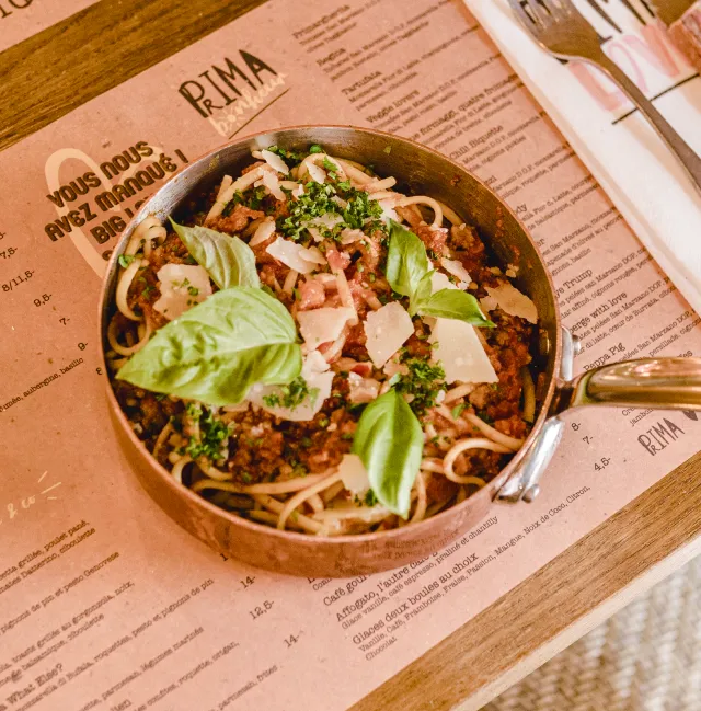 Plat de pâtes dans une cassolette en fonte posée sur une carte du restaurant Prima Bonheur