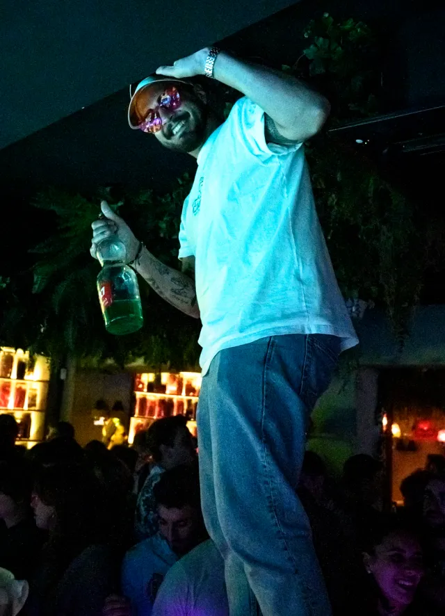 Homme debout sur le bar, une bouteille de Get27 à la main